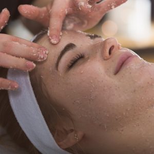 Beautician applying exfoliating salt scrub on woman's face